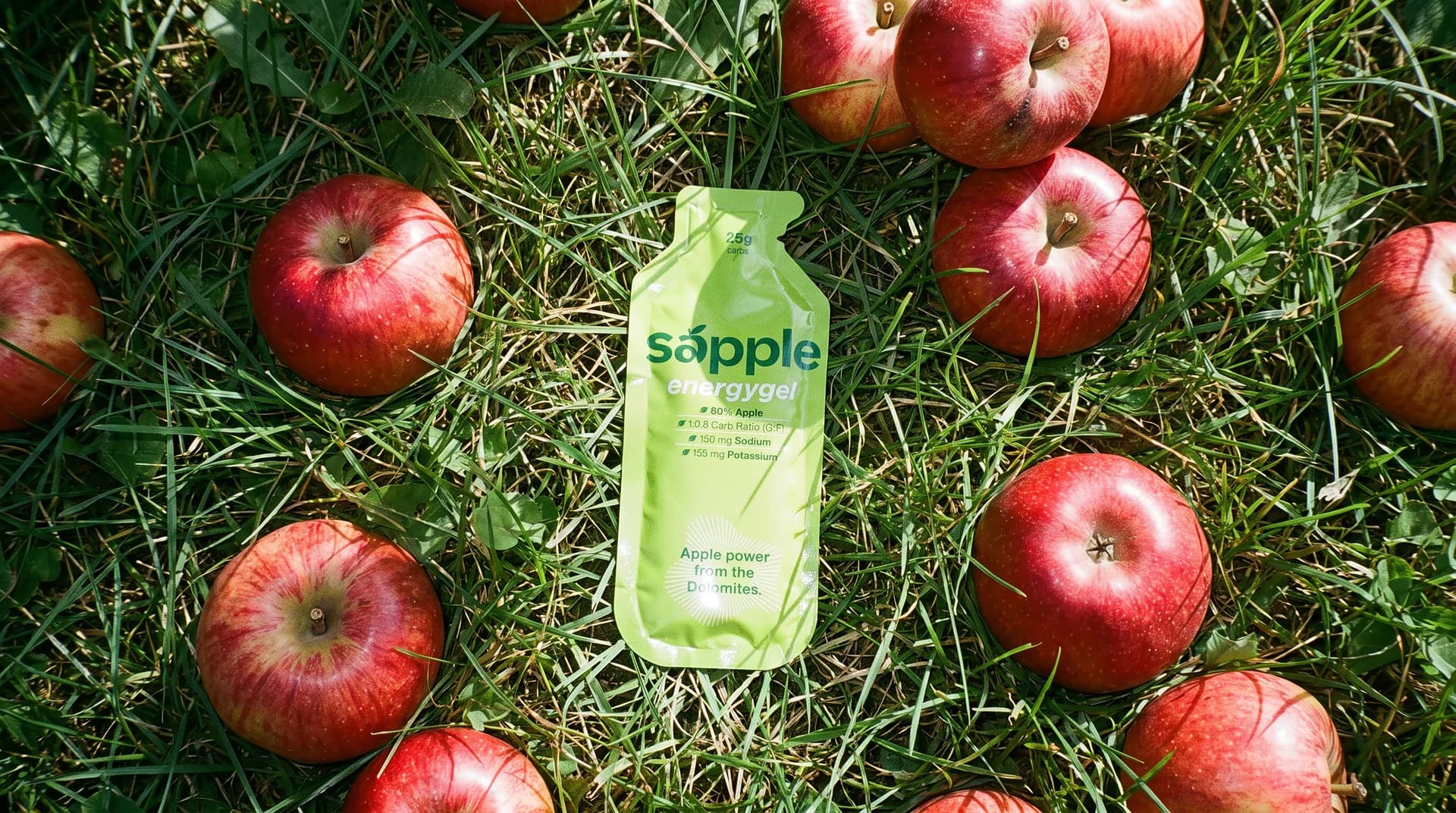 sapple Power organic energy gel made from South Tyrolean apple, lying in the grass between fresh apples